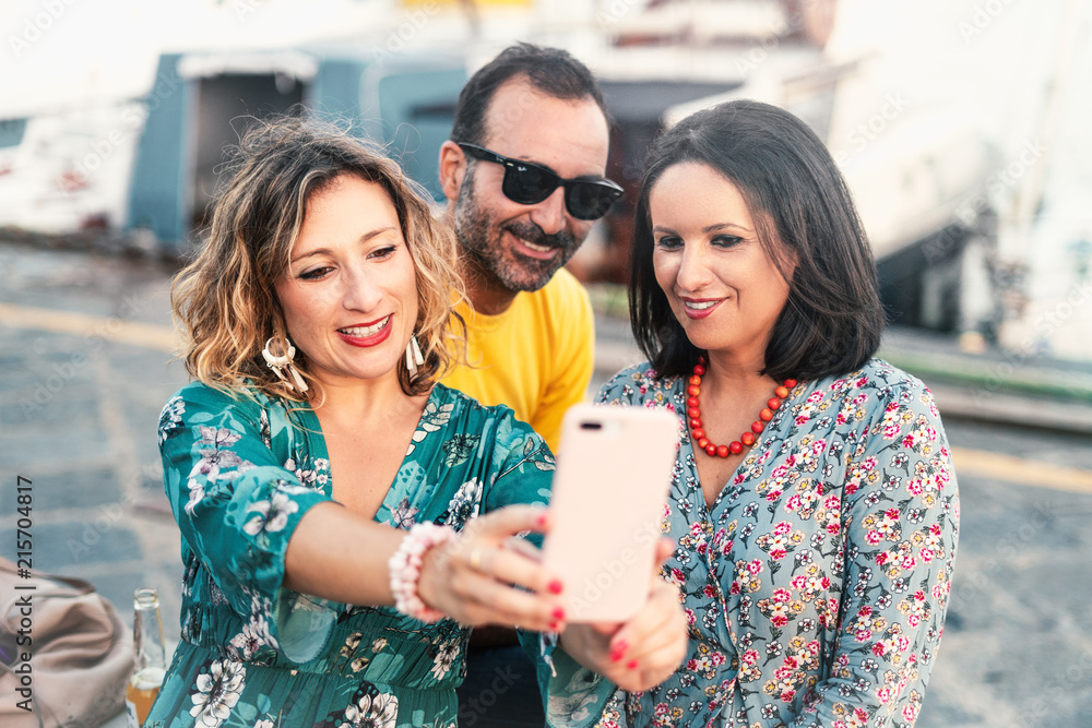 Wall mural portrait of three friends (two woman and a man) taking photos with a smartphone in outdoor