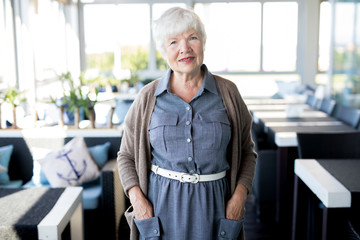 Waist up portrait of modern senior woman looking at camera and smiling while posing in cafe