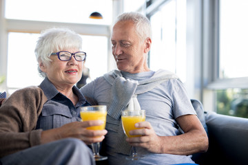 Portrait of modern senior couple embracing and holding glasses with fresh orange juice while...