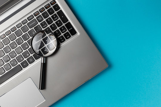 Laptop computer with magnifying glass on blue background, concept of search. Internet security conceptual image. Top view. Flat lay