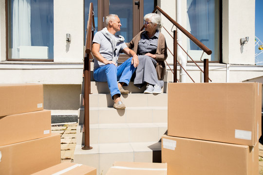 Portrait of happy senior couple sitting on porch of new house with cardboard boxes in foreground, copy space