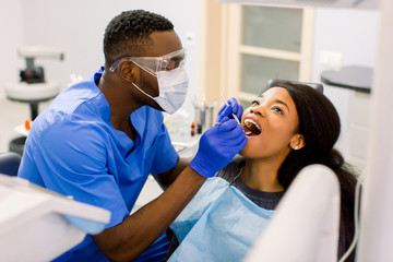 Close-up portrait of the african young woman patient examining by male dentist with tools in dental...