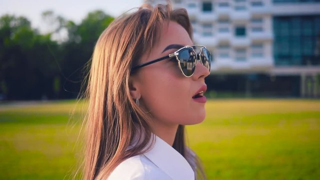 Good-looking young Caucasian woman in sunglasses walking through the street. Portrait of nice fashionable Slavic girl. Close-up. Summertime.
