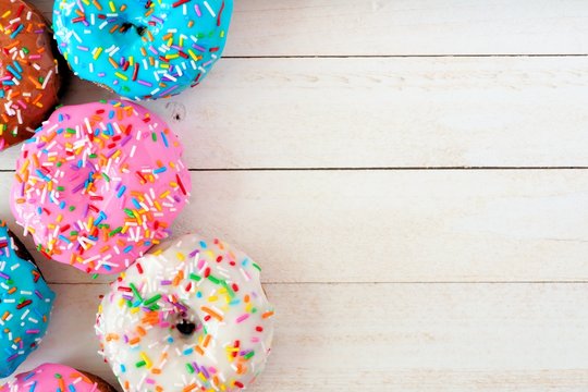 Side border of assorted donuts with pastel colored icing and sprinkles against a white wood background