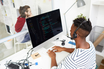 Serious busy African-American IT engineer in hands free device solving problem remotely and working with computer in office
