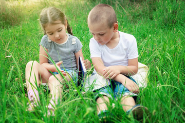 Children sit on the grass on a sunny day and read a book. Preparation for school