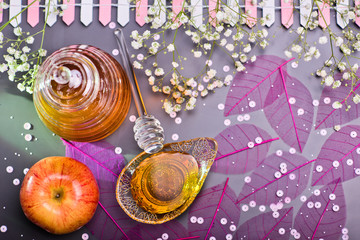 Rosh Hashanah Jewish holiday concept - red yellow apple, glass dipper on saucer of honey, Honey jar on grey background and white flowers. Traditional holiday symbols