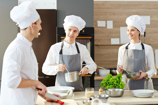 Team of cooks talking at work: group of young cooks in uniform preparing pasta together and carrying out different work