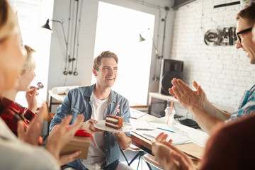 Portrait of creative young people celebrating Birthday in office, focus on handsome man receiving cake and laughing, copy space