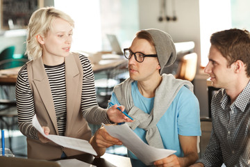 Team of  three creative business people discussing startup project  at meeting table, holding documents while working in modern office