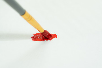 Paintbrush dipped in red color making stain on the paper, up close macro shot isolated on white background.