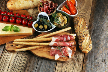 Italian antipasti wine snacks set. Cheese variety, Mediterranean olives, crudo, Prosciutto di Parma, salami and wine in glasses over wooden grunge background.