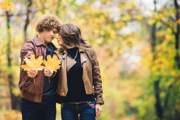 Loving happy couple in autumn in park holding autumn maple leaves in hands.