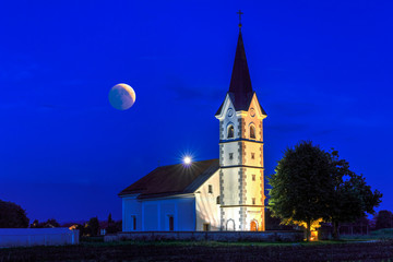 St. Florian church with a view of the lunar eclipse (July 27th 2018) in the evening on a field near Menges, Slovenia - obrazy, fototapety, plakaty