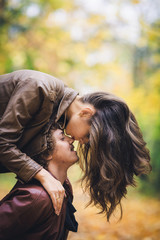 Young loving couple in autumn in park. Girl kisses guy in nose.
