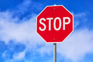 Red stop sign against blue cloudy sky background. Traffic regulatory warning sign.