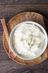 White bowl with sour cream or homemade yogurt on a wooden tray, top view.