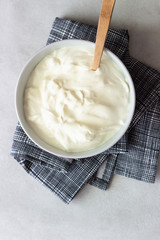 Sour cream or homemade yogurt in a bowl on light grey background. Top view, copy space.