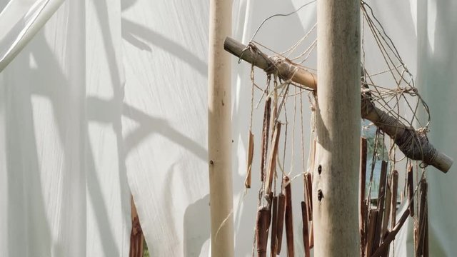White linen cloth and ethnic dreamcatcher on wooden poles swings in the wind. Against the blue sky and green trees and fields.