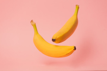 Two yellow bananas levitate in air on pink background.