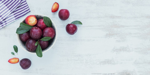 Naklejka na ściany i meble Fresh plums with leaves on rustic wooden table background.