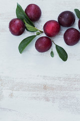 Fresh plums with leaves on white rustic wooden table background.