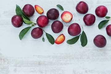 Naklejka na ściany i meble Fresh plums with leaves on white rustic wooden table background.