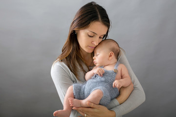 Young mother, caressing her newborn baby boy, holding him in her arms and smiling