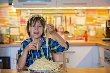Little preschool boy, cute child, eating spaghetti for lunch and making a mess