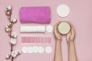 Spa concept. Cosmetic cream for face and body with woman hands, cotton branch, cotton pads, ear sticks, pink towel. Cotton Cosmetic Makeup Removers Tampons. Flat lay background Top view