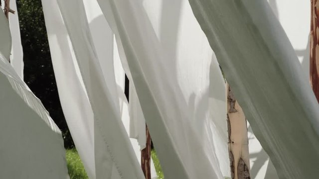 White linen cloth on wooden poles swings in the wind. Against the blue sky and green trees and fields.
