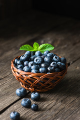 Blueberries in basket on wooden table. Freshly picked blueberries. Low key, dark food photo. Summer harvest. Selective focus