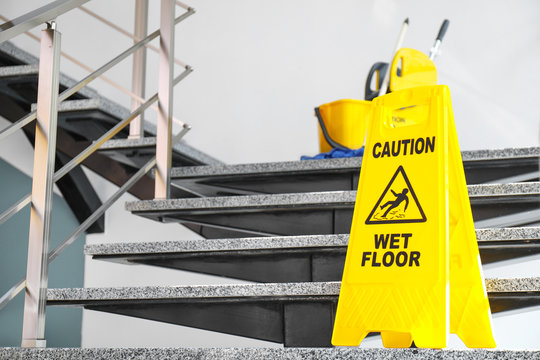 Safety sign with phrase Caution wet floor and mop bucket on stairs. Cleaning service