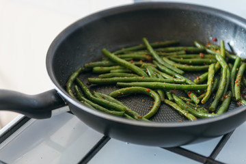 Frozen green beans in frying pan, salt, pepper and vegetable oil