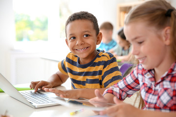 Cute little children with gadgets sitting at desk in classroom. Elementary school