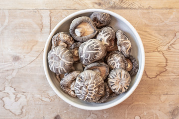 Small bowl of mixed dried shiitake mushrooms on a weathered table top, horizontal aspect