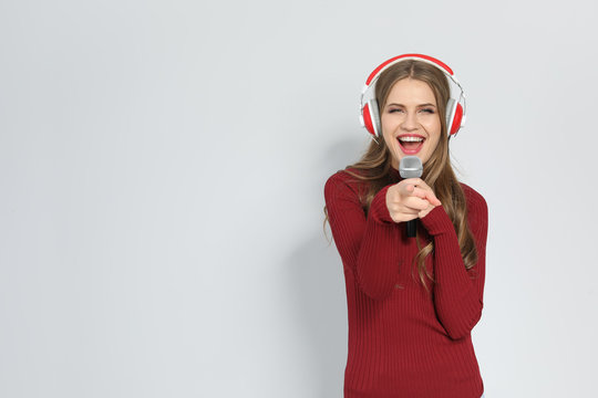 Young woman singing into microphone on color background. Christmas music