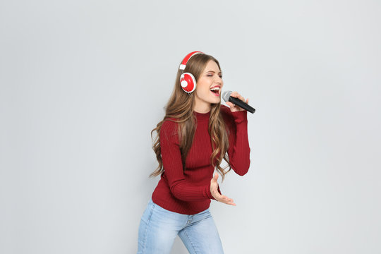 Young woman singing into microphone on color background. Christmas music