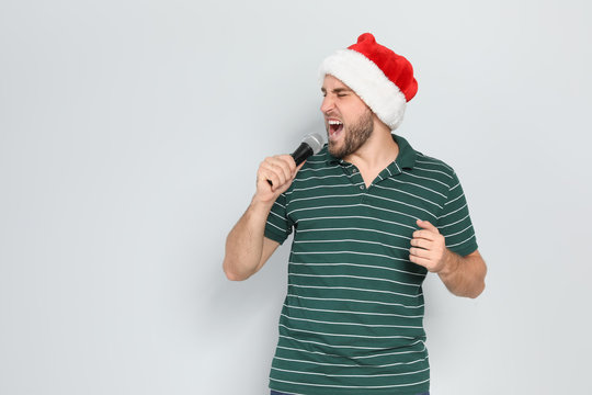Young man in Santa hat singing into microphone on color background. Christmas music