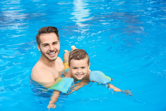 Father teaching son to swim with inflatable sleeves in pool on sunny day