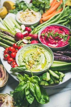 Healthy raw summer vegan snack plate. Chickpea, beetroot, spinach hummus dips with colorful fresh vegetables and greens on white table background. Clean eating, dieting, vegan or vegetarian party food