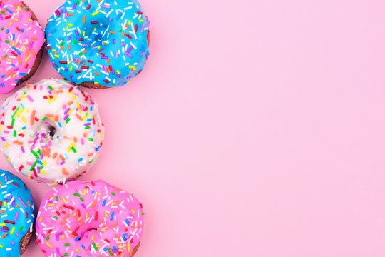 Side border of assorted donuts with frosting and sprinkles against a pastel pink background