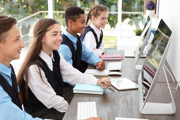 Teenage students in stylish school uniform at desks with computers - obrazy, fototapety, plakaty