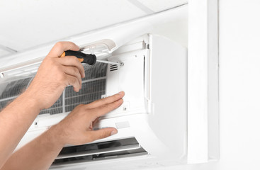 Male technician fixing modern air conditioner indoors