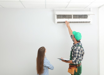 Male technician speaking with woman about air conditioner indoors