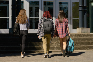 Group of female students walking in front of school with backpacks