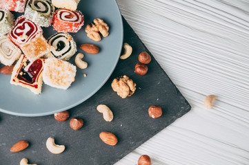 Traditional oriental sweets and nuts: hazelnuts, cashews on a white wooden background. Turkish dessert is the locus of Rahat. View from above. Place under the text.