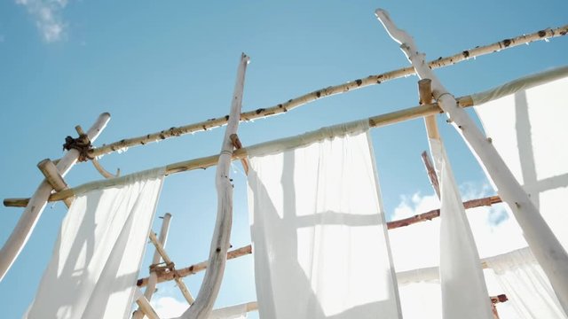 White linen cloth on wooden poles swings in the wind. Against the blue sky and green trees and fields.
