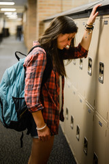 Sad high school student leaning against locker with backpack