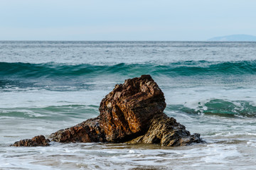 Wave cresting behind rock near the beach of Crystal Cove State Park in Laguna Beach, California. Foam from an earlier wave is in the foreground  Pacific ocean is in the background. © dhayes